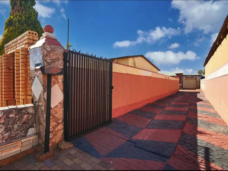 A gated entrance featuring a paved driveway leading to a garage, enclosed by brick boundary walls with decorative tiling.