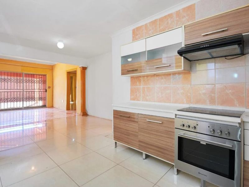 Open-plan kitchen and living area featuring tiled flooring, built-in cabinetry, and decorative columns leading to a secure patio space.
