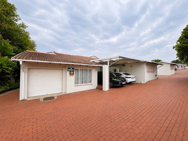 Front exterior view of a townhouse featuring a single garage, covered carport, and paved driveway in a well-maintained residential complex.