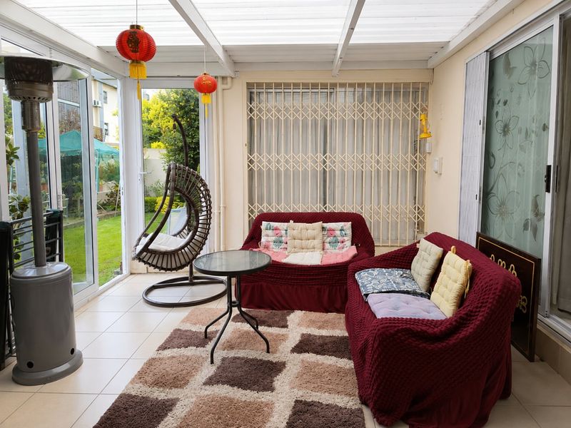 A covered patio area featuring tiled flooring, a translucent roof, and sliding glass doors providing access to the garden.