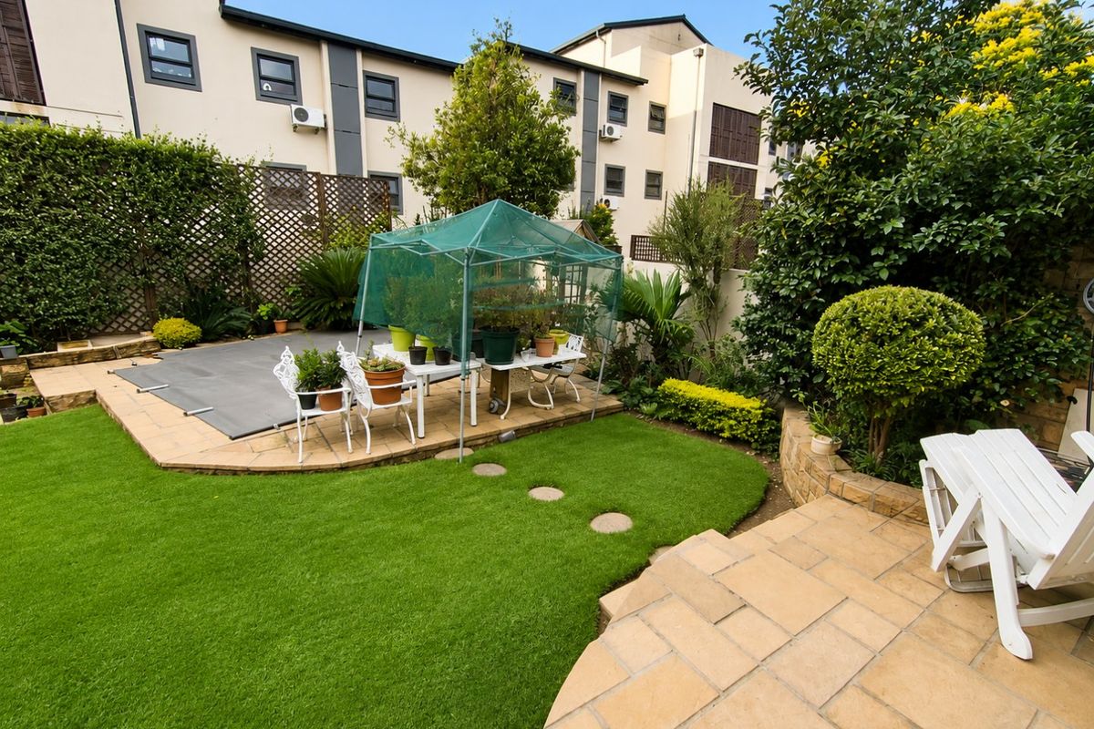 A well-maintained rear garden featuring a paved patio area, artificial lawn, and a swimming pool with a safety cover.