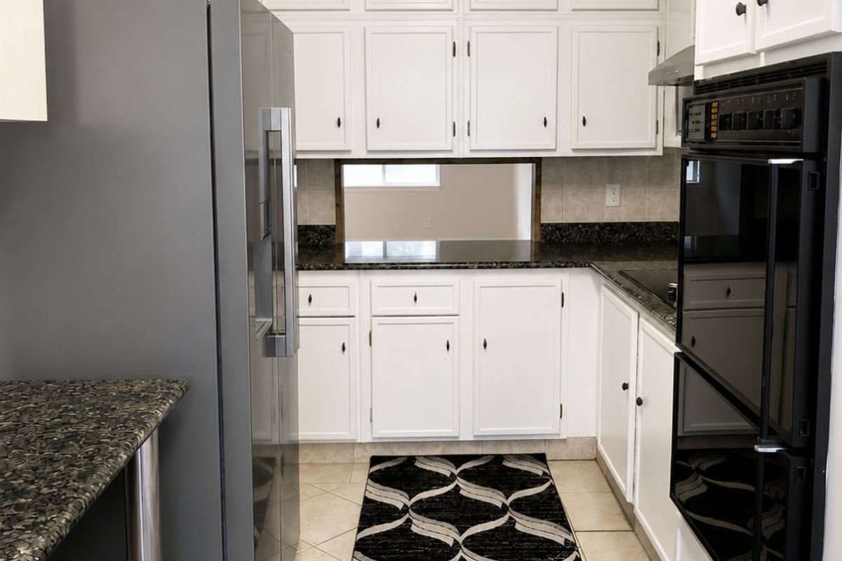 A functional kitchen featuring white cabinetry, granite countertops, a double wall oven, and a convenient pass-through window connecting to the adjacent living space.