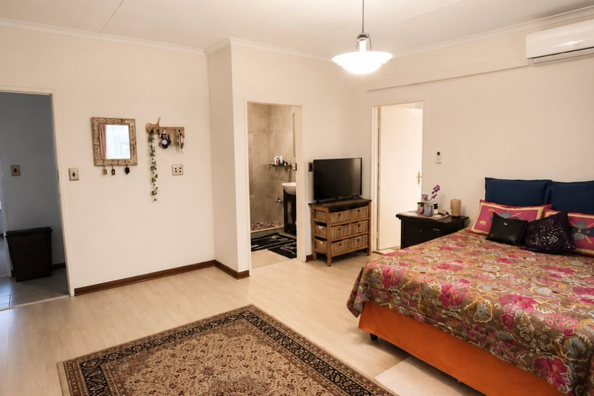 Spacious bedroom featuring laminate flooring, an en-suite bathroom, and a wall-mounted air conditioning unit.