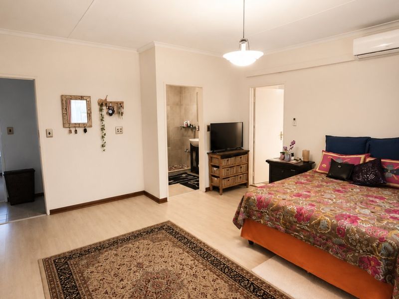 Spacious bedroom featuring laminate flooring, an en-suite bathroom, and a wall-mounted air conditioning unit.