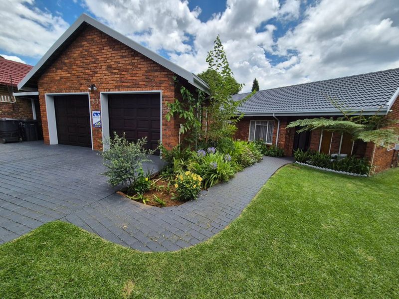Front view of a well-maintained brick house featuring a double garage, paved driveway, and a neat landscaped garden.