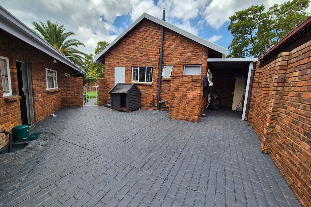 A well-maintained rear courtyard featuring dark brick paving, a brick exterior facade, and a covered carport area.