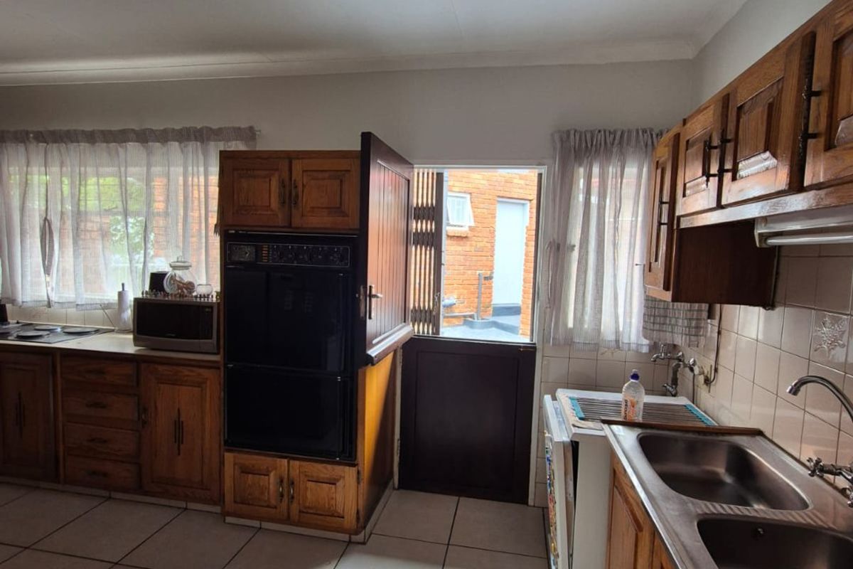 A functional kitchen featuring traditional wooden cabinetry, double stainless steel sink, built-in eye-level oven, and tiled flooring with direct access to the exterior.