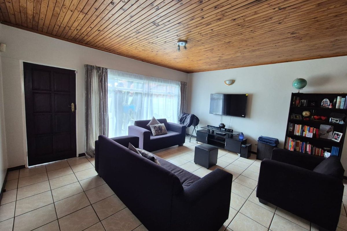 A living room featuring ceramic floor tiles and a distinctive timber tongue and groove ceiling, providing a dated but functional living space.