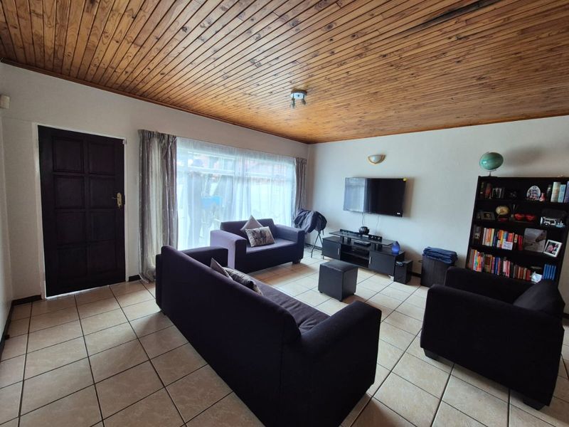 A living room featuring ceramic floor tiles and a distinctive timber tongue and groove ceiling, providing a dated but functional living space.