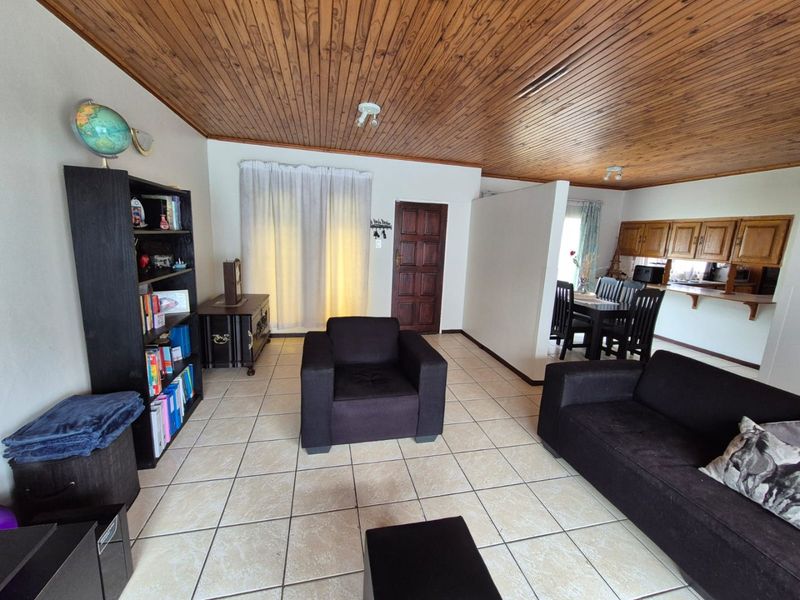 Open plan living and dining area featuring ceramic tiled flooring and a timber tongue and groove ceiling, with an adjoining kitchen space.