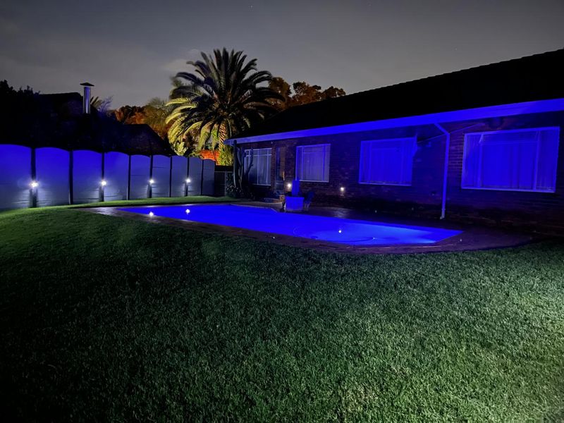 Night view of a residential backyard featuring a swimming pool with blue underwater lighting and exterior wall illumination.
