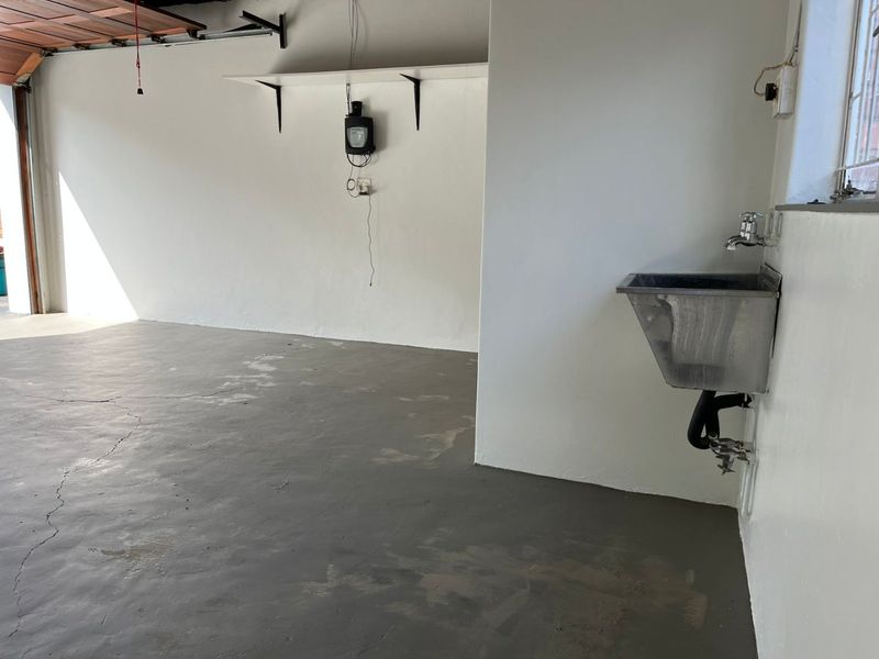 A spacious, empty garage featuring a concrete floor with visible cracking, a wall-mounted stainless steel utility sink, and overhead garage door infrastructure.
