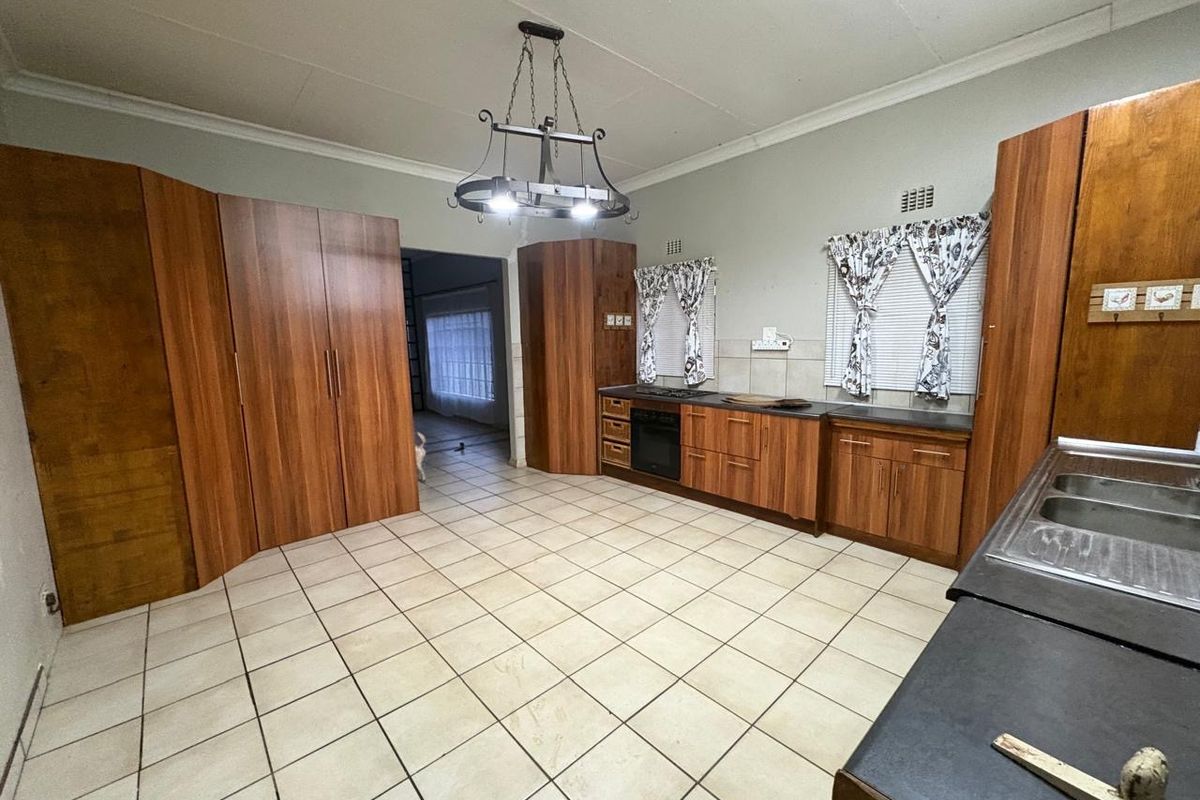 Spacious kitchen featuring wood-finish cabinetry, built-in oven and hob, double sink, and tiled flooring, offering a functional layout with potential for modern updates.