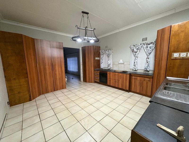 Spacious kitchen featuring wood-finish cabinetry, built-in oven and hob, double sink, and tiled flooring, offering a functional layout with potential for modern updates.