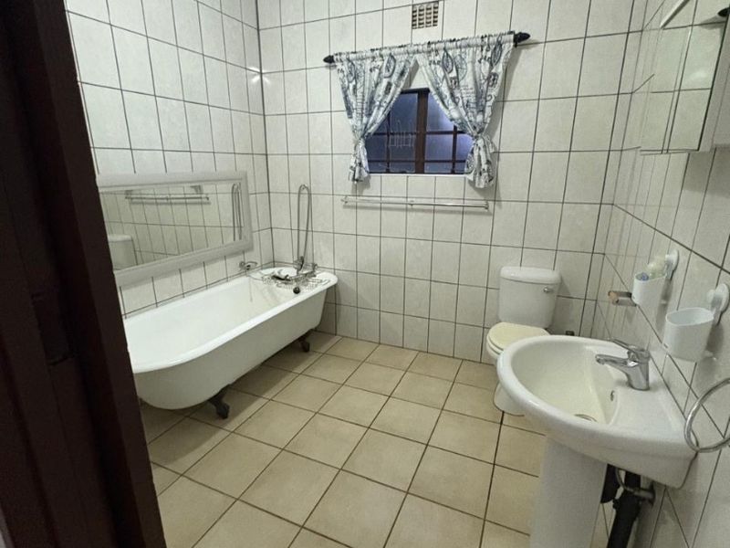A traditional bathroom featuring a classic clawfoot bathtub, pedestal basin, and full-height wall tiling with a crystal chandelier fixture.