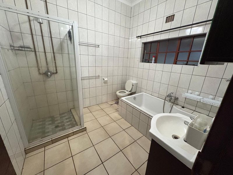 A functional bathroom featuring a separate shower enclosure, bathtub, toilet, and washbasin with fully tiled walls and flooring.