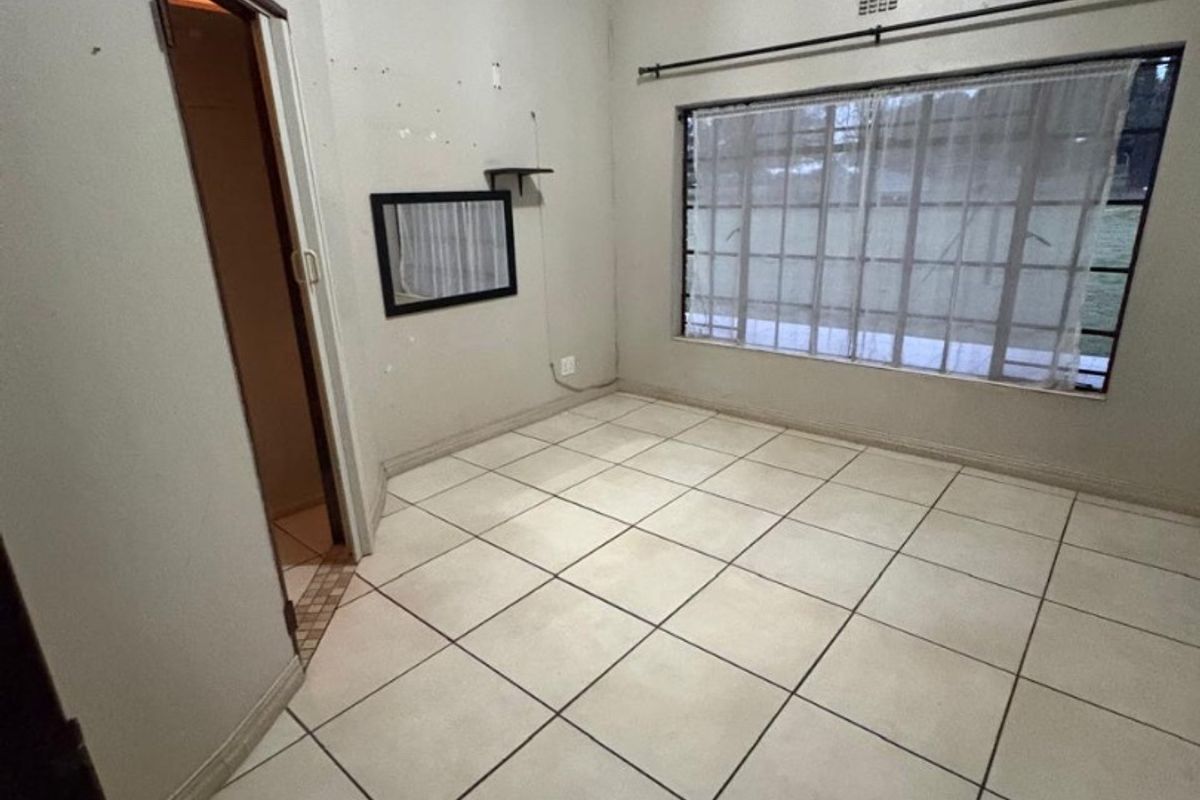 An empty bedroom featuring tiled flooring, a large window with security bars, and cove cornicing, ready for renovation or staging.