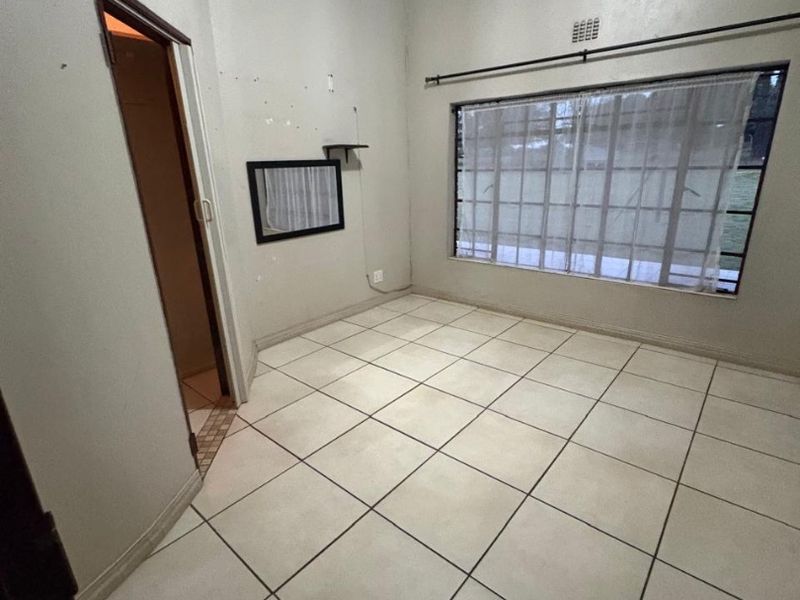 An empty bedroom featuring tiled flooring, a large window with security bars, and cove cornicing, ready for renovation or staging.