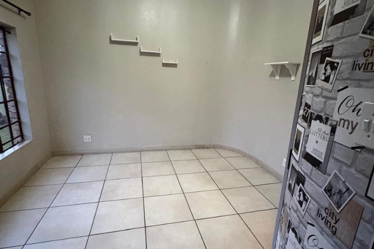 An empty living area featuring neutral tiled flooring, coved ceilings, and wall-mounted shelving, offering a blank canvas for interior design.