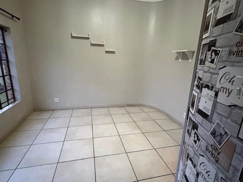 An empty living area featuring neutral tiled flooring, coved ceilings, and wall-mounted shelving, offering a blank canvas for interior design.