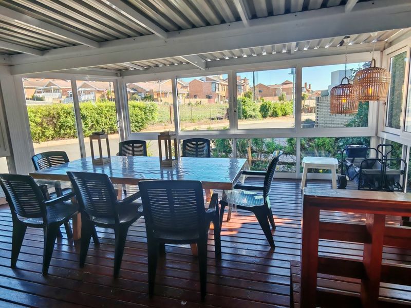 A bright, enclosed patio featuring timber decking, a corrugated metal roof, and large glass windows providing views of the surrounding neighborhood.