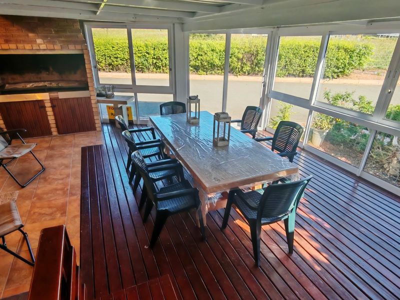 Enclosed patio featuring timber decking, tiled flooring, and a built-in brick braai, providing a versatile outdoor entertainment space with garden views.