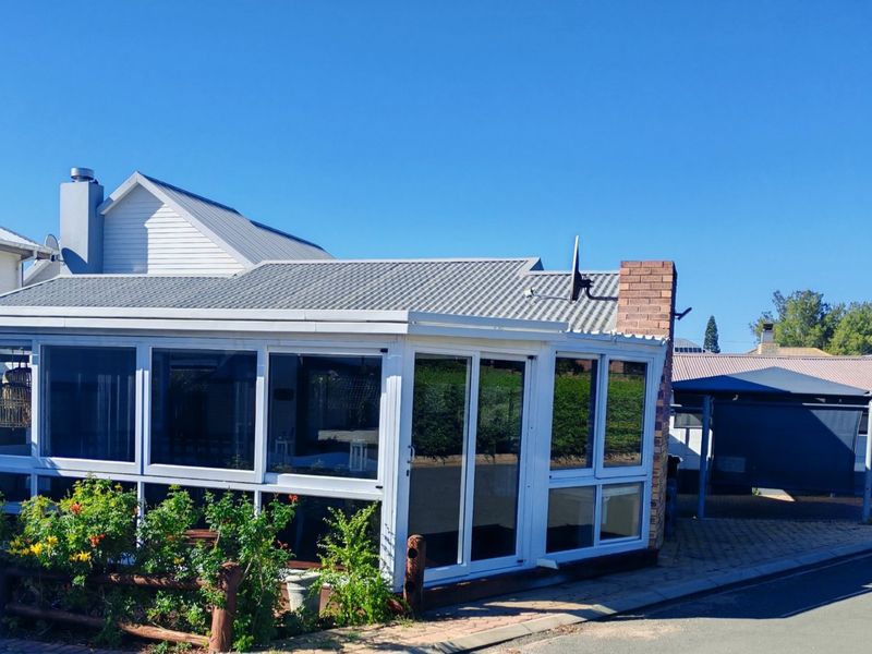 Front view of the property featuring an enclosed patio with aluminium frames, tiled roofing, and a brick chimney, set against a paved driveway.
