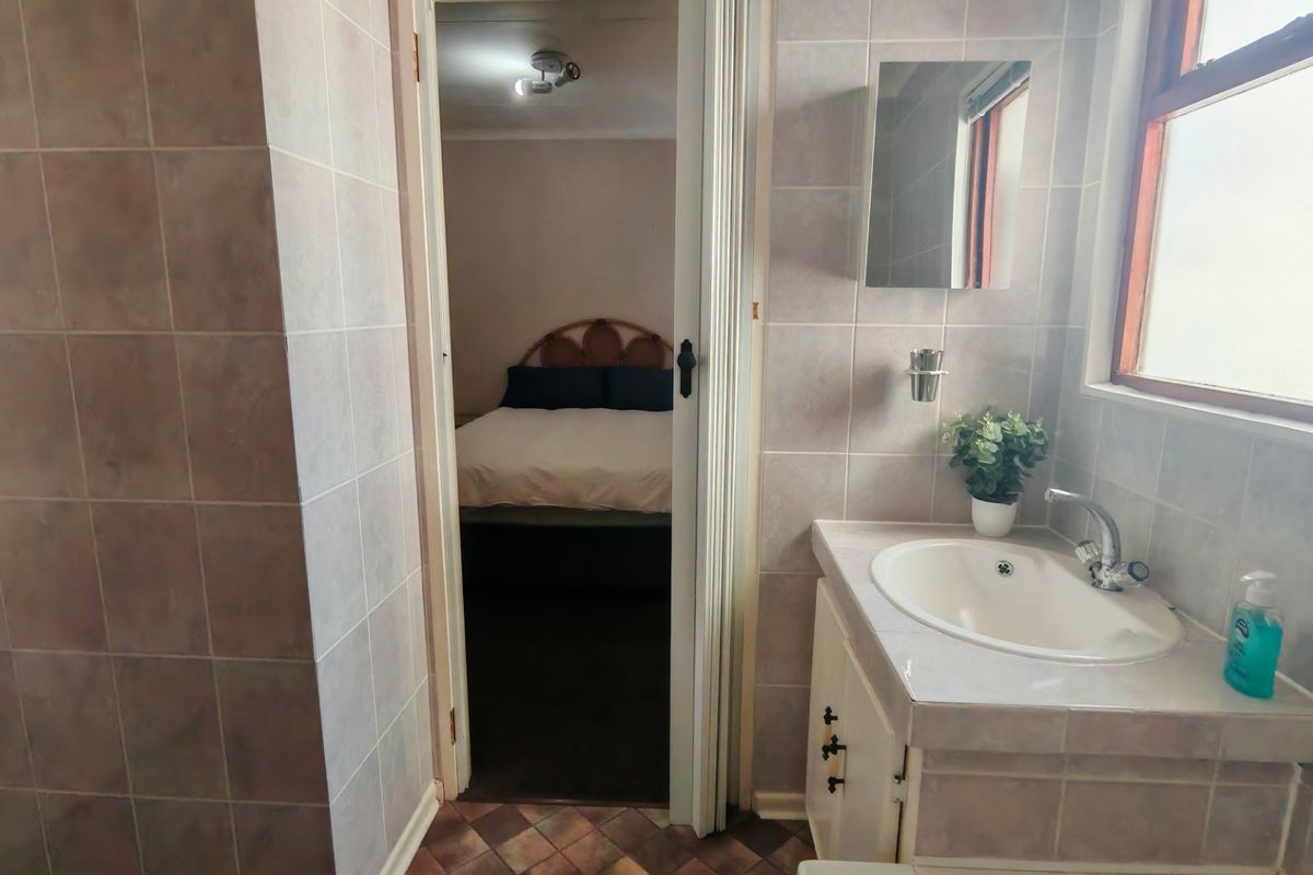 A functional bathroom featuring tiled walls, a vanity cabinet with an integrated sink, and a view into the adjacent bedroom.