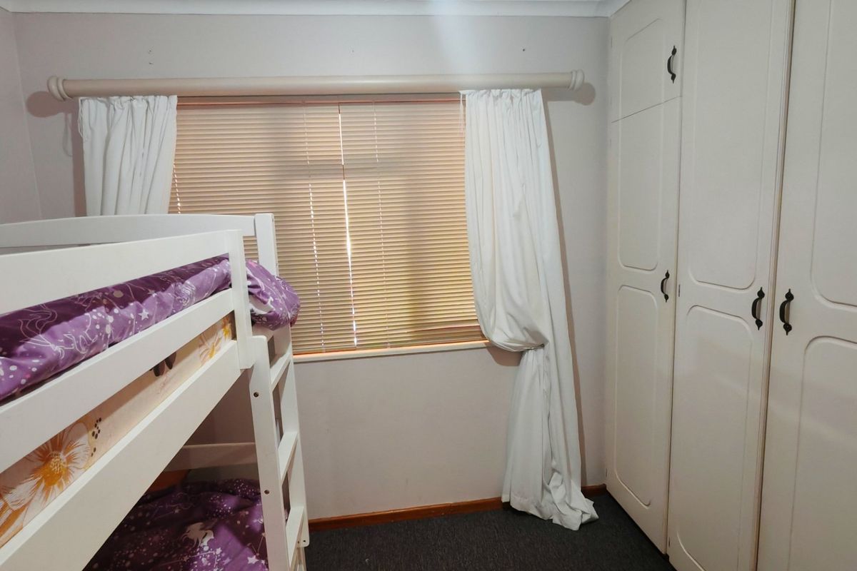 A functional bedroom featuring built-in cupboards and a window fitted with venetian blinds and a curtain rod.