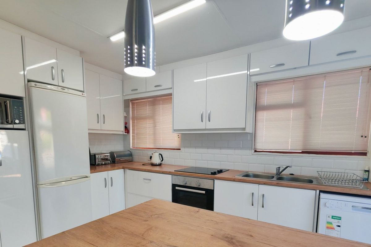 A well-maintained kitchen featuring white cabinetry, wooden countertops, subway tile backsplash, and integrated appliances including an oven and hob.