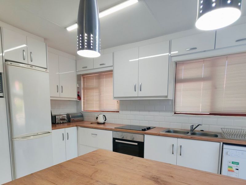 A well-maintained kitchen featuring white cabinetry, wooden countertops, subway tile backsplash, and integrated appliances including an oven and hob.