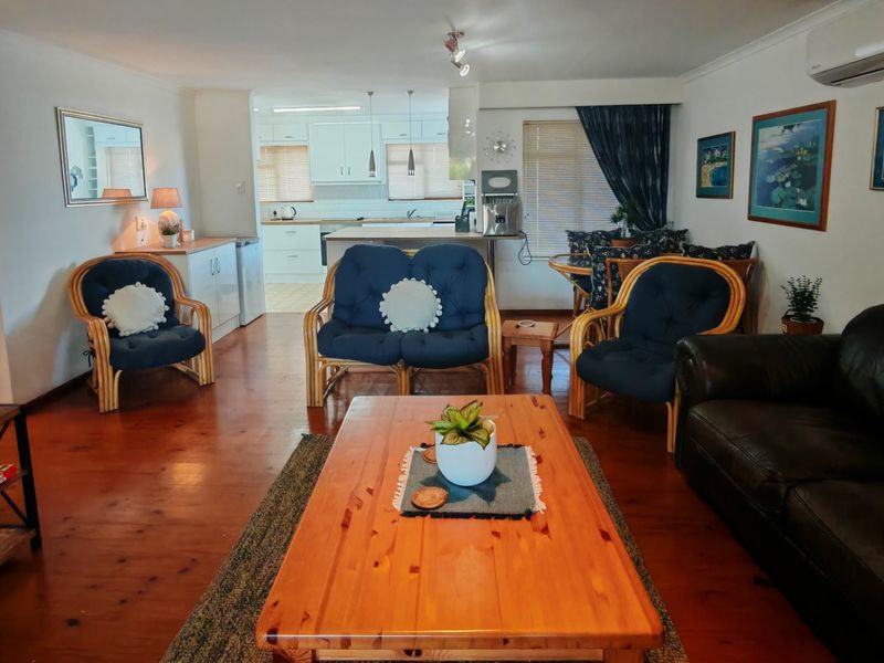 Open plan living and kitchen area featuring warm timber flooring, neutral walls, and a functional kitchen layout with island bench.