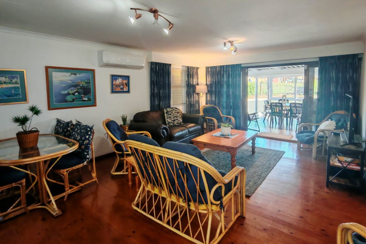Spacious living room featuring polished hardwood flooring, a wall-mounted air conditioning unit, and large sliding glass doors providing access to the outdoor patio area.