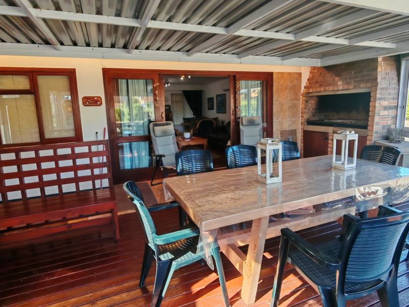 Covered outdoor patio featuring timber decking, a built-in brick braai, and direct access to the interior living space through sliding glass doors.
