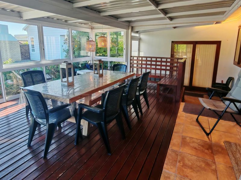 A spacious enclosed patio featuring timber decking, tiled flooring, and large windows, providing a versatile outdoor entertainment area.