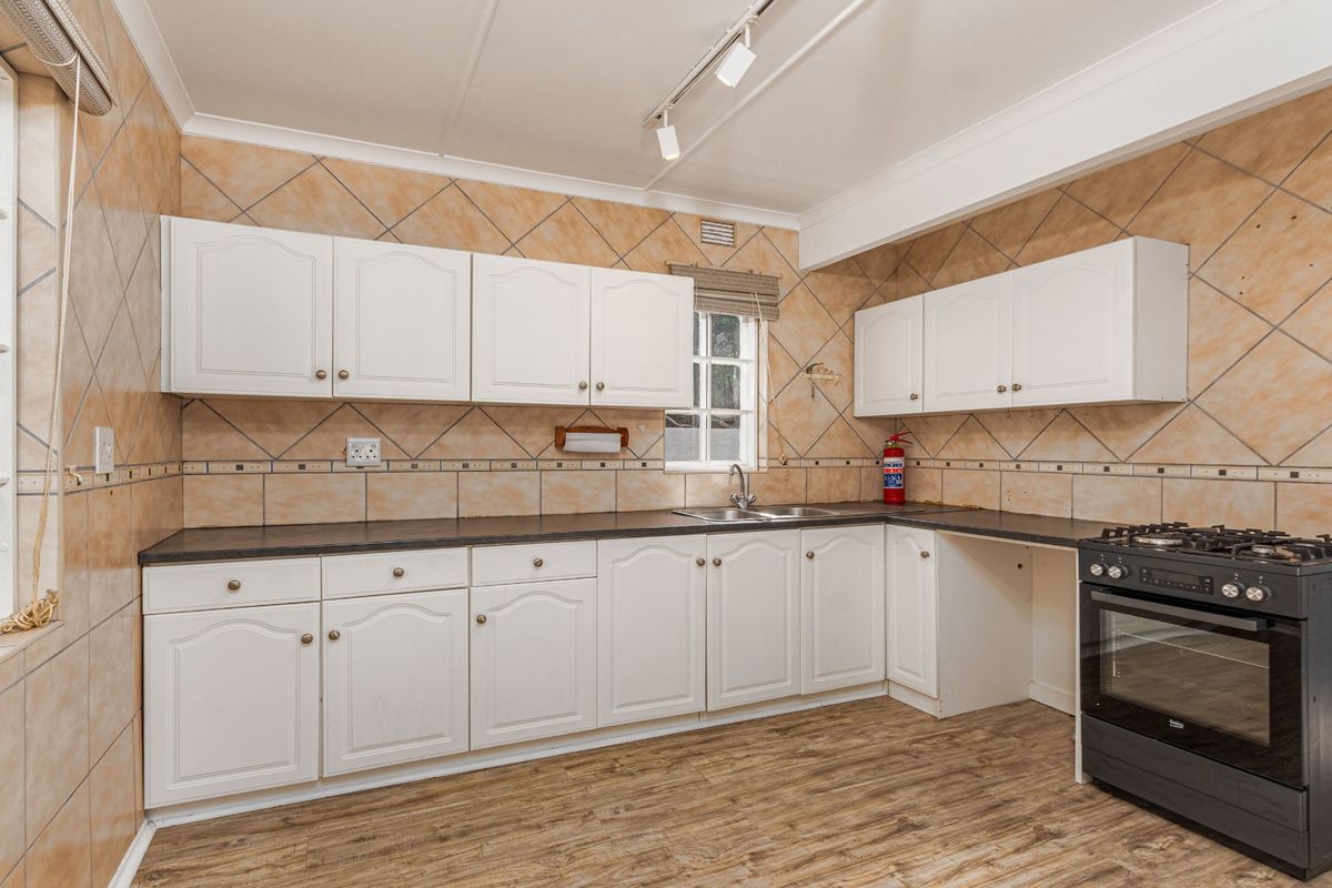 A functional kitchen featuring white cabinetry, laminate countertops, a stainless steel sink, and a freestanding oven, complemented by tiled splashbacks and track lighting.