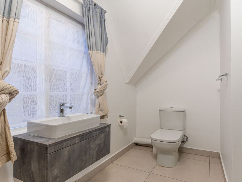 A clean and modern bathroom featuring a wall-mounted vanity with a countertop basin, a toilet, and neutral floor tiling under a sloped ceiling.