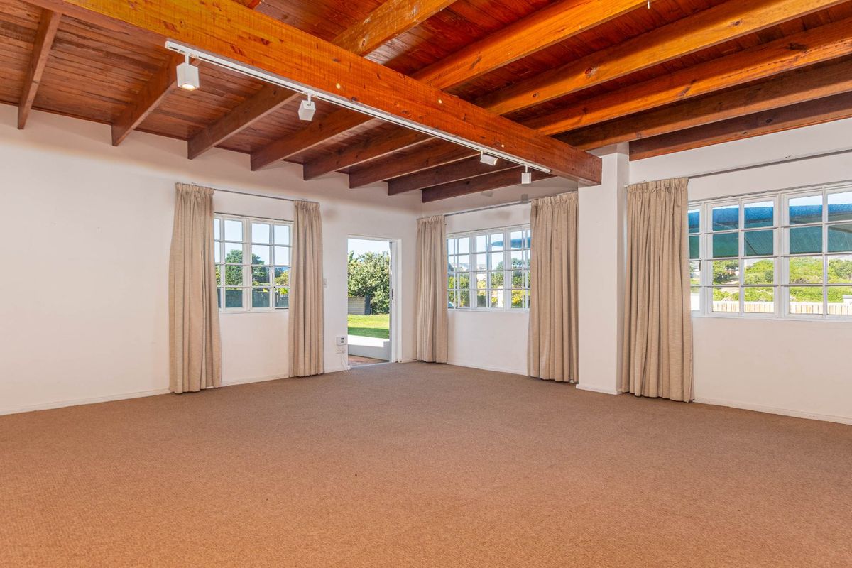 Spacious living area featuring exposed timber beam ceilings, neutral carpeting, and multiple windows providing natural light and direct access to the garden.