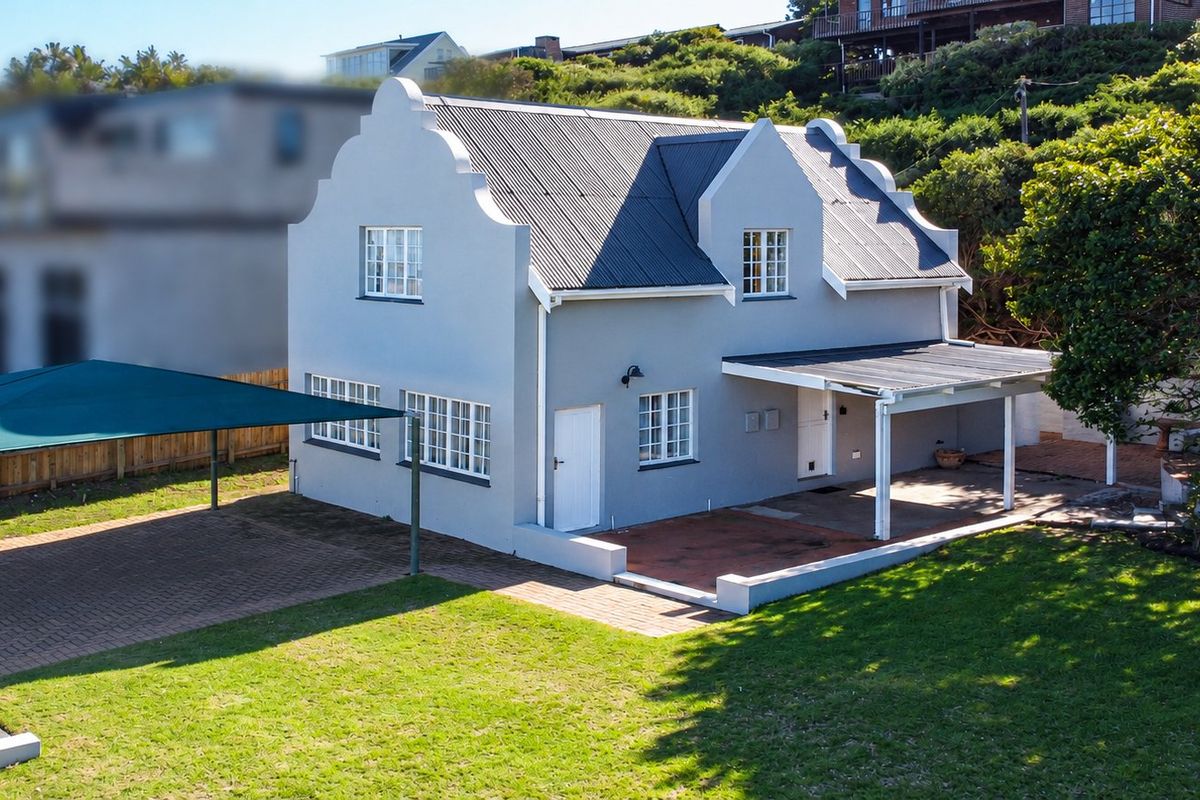 A well-maintained two-story house featuring a gabled roof, covered patio area, paved driveway with shade sail, and a spacious surrounding garden.