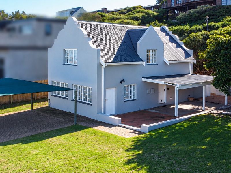 A well-maintained two-story house featuring a gabled roof, covered patio area, paved driveway with shade sail, and a spacious surrounding garden.