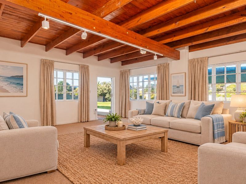A bright and inviting living room featuring exposed timber ceiling beams, track lighting, and large multi-pane windows that provide ample natural light.