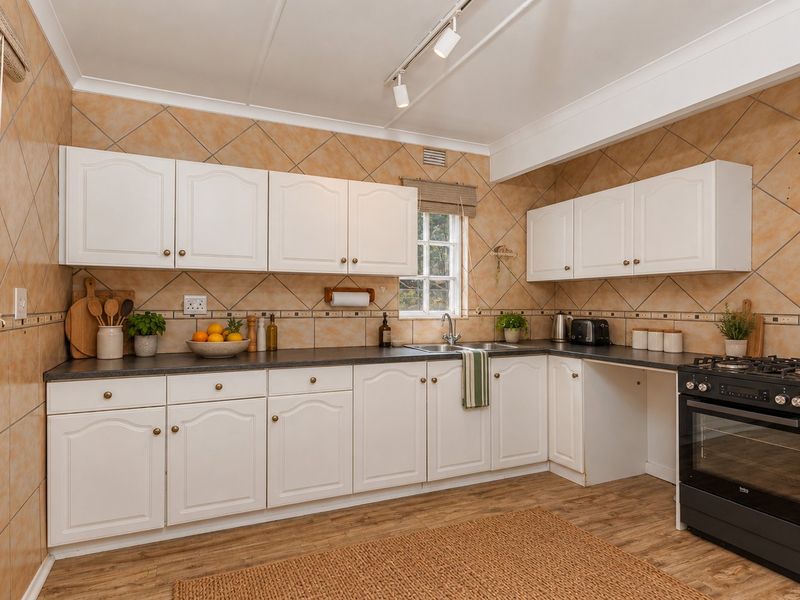 A functional kitchen featuring white cabinetry, dark laminate countertops, a stainless steel sink, and a freestanding oven with a tiled splashback.