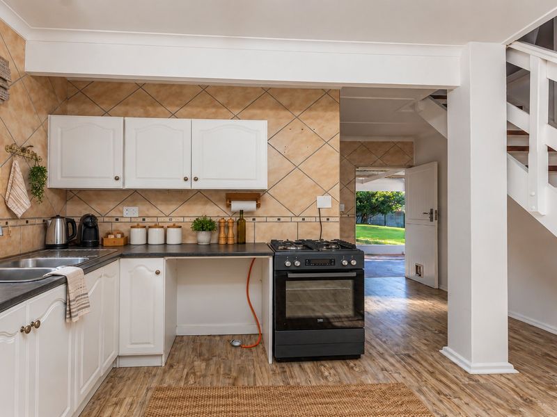 A functional kitchen featuring white cabinetry, a gas stove, and tiled backsplash, with an open-plan layout leading to a staircase and rear garden access.