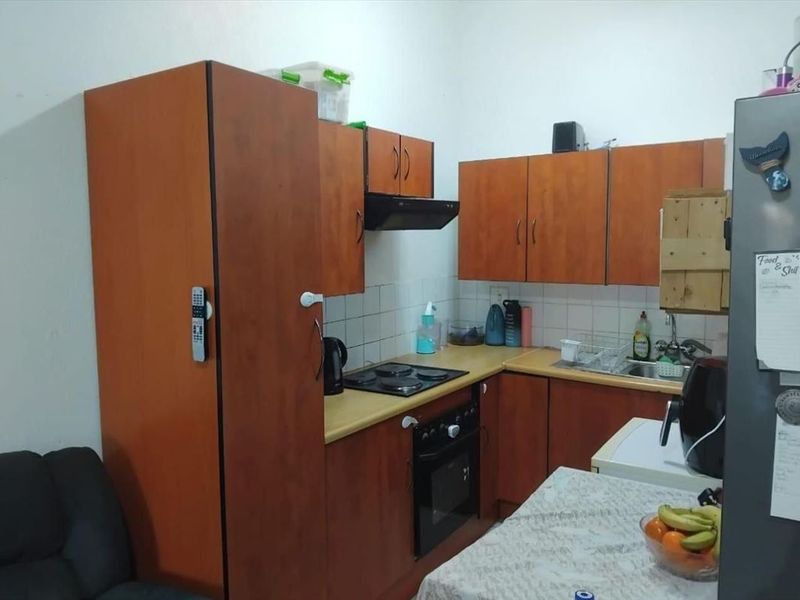 A compact kitchen featuring wood-look laminate cabinetry, a built-in oven with electric hob, and a tiled backsplash.