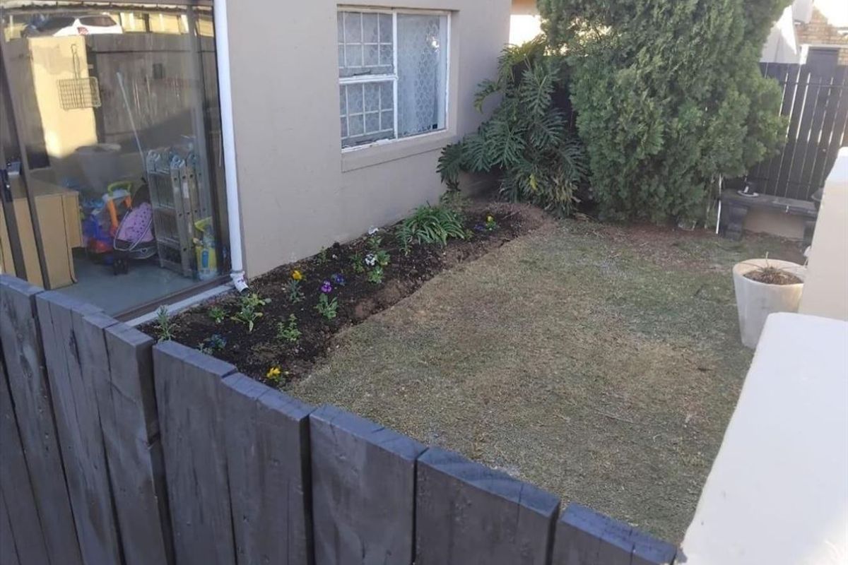 A rear garden area featuring a small lawn, a flower bed, and a sliding glass door providing access to the townhouse interior.