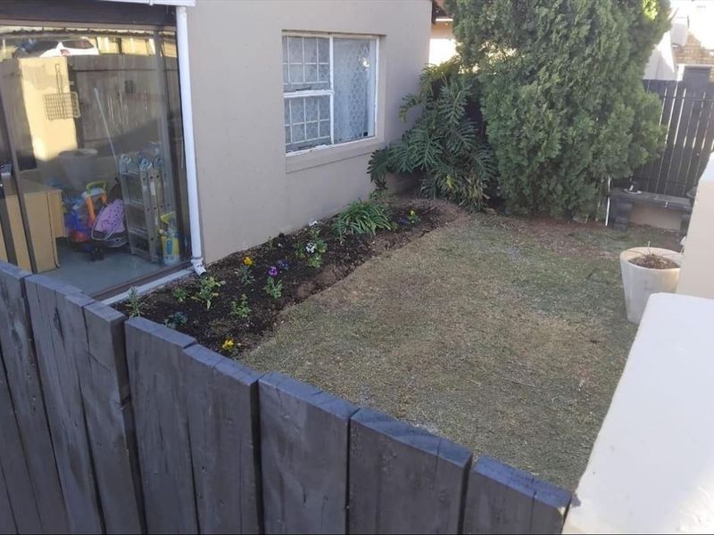 A rear garden area featuring a small lawn, a flower bed, and a sliding glass door providing access to the townhouse interior.