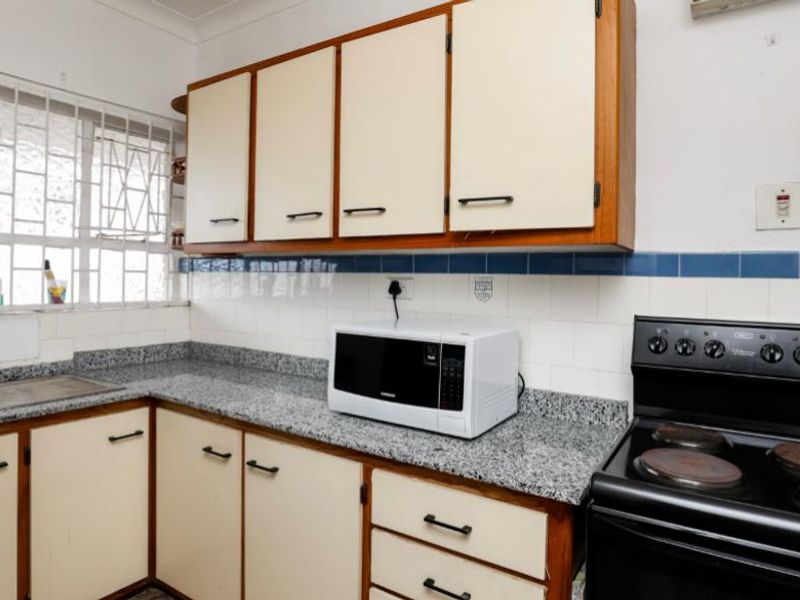 A functional kitchen featuring granite countertops, built-in cabinetry, and a freestanding electric stove, offering a practical layout with potential for modern updates.