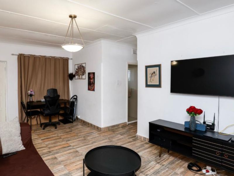 A living room featuring tiled flooring, cove cornicing, and a central pendant light fixture, providing a functional and well-lit living space.