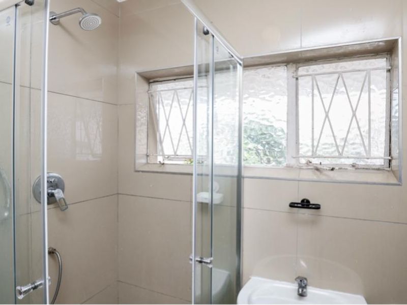 A functional bathroom featuring a glass shower enclosure, wall-mounted basin, and tiled walls with a window providing natural light.
