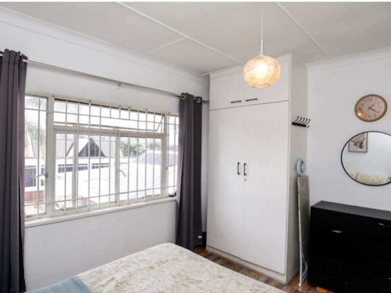 A functional bedroom featuring a built-in wardrobe, security bars on the window, and neutral finishes, offering a practical space for residents.